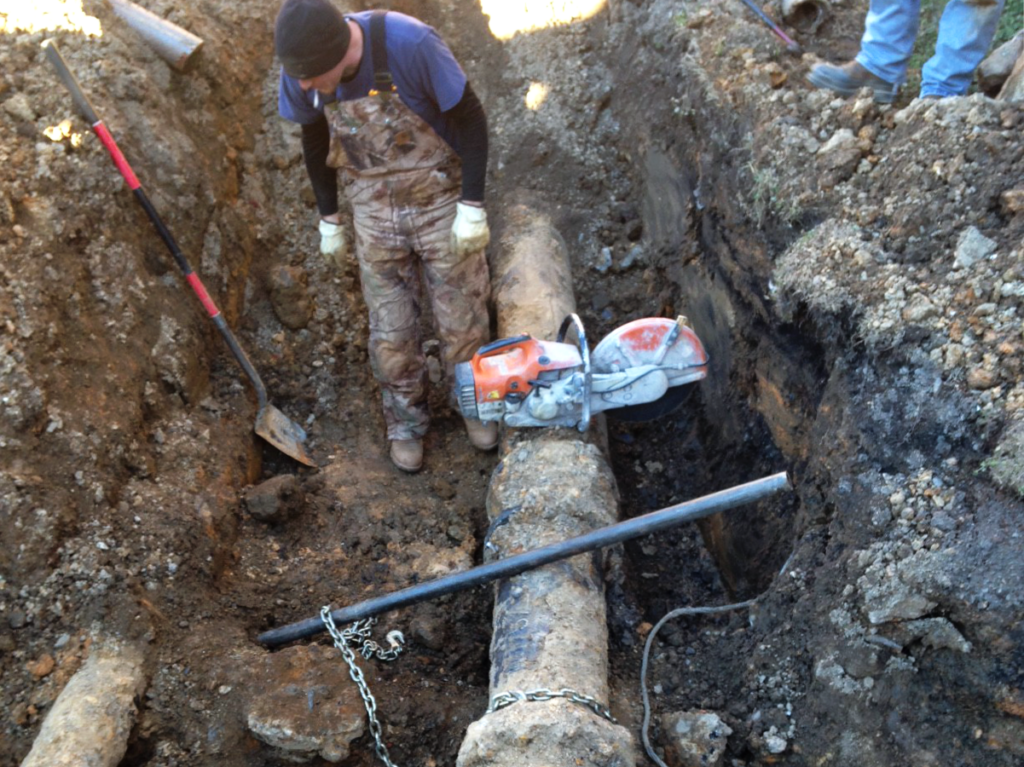 An employee unearthing a large underground pipe.