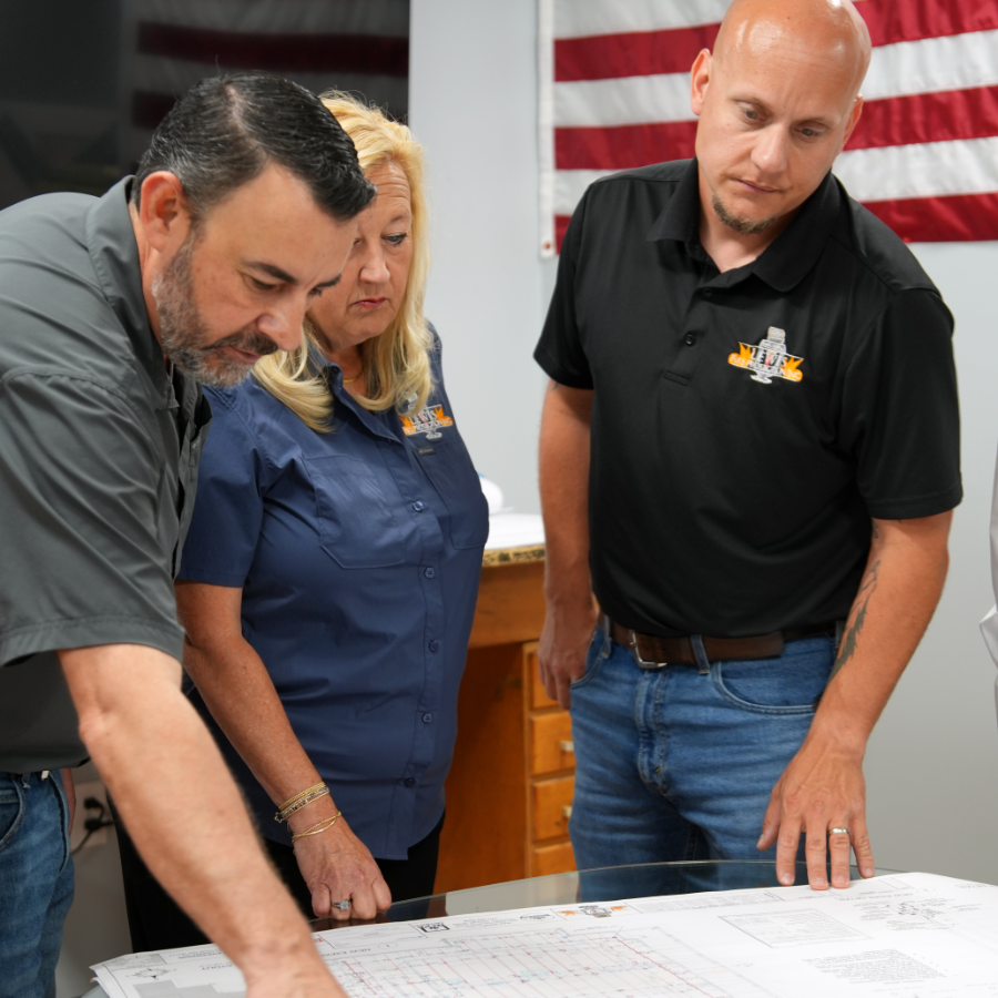 Employees gathered around a table, pointing at a blueprint, while discussing a project.