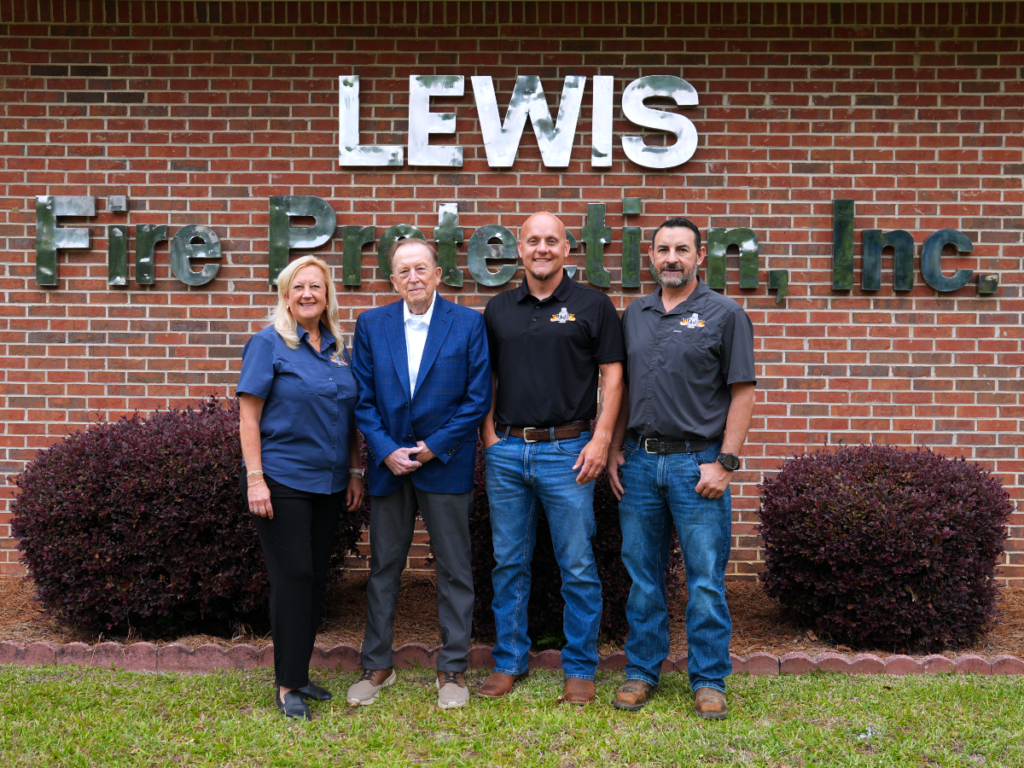 The office staff of Lewis Fire Protection standing in front of their building sign.